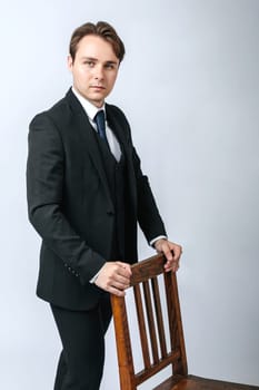 Business and finance concept. Portrait of a businessman in a black suit near the chair. Light background