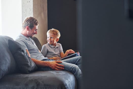 Sitting on the sofa. Father and son is indoors at home together.