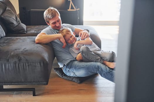 Having free time. Father and son is indoors at home together.