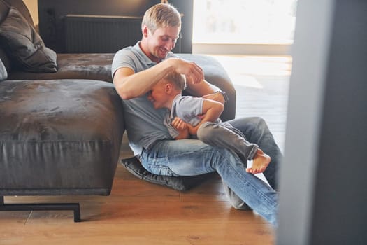 Having free time. Father and son is indoors at home together.