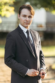 Business and finance concept. Portrait of a businessman holding glasses in his hands. In the park