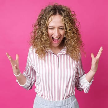 A curly-haired woman raises her palms in joy, glad to receive an amazing gift from someone, screams loudly, wearing a striped shirt. Isolated on a purple background.
