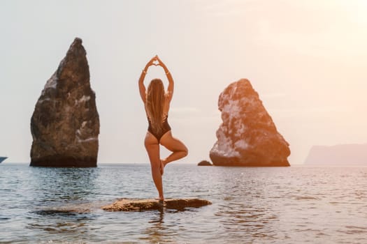 Woman meditating in yoga pose silhouette at the ocean, beach and rock mountains. Motivation and inspirational fit and exercising. Healthy lifestyle outdoors in nature, fitness concept.