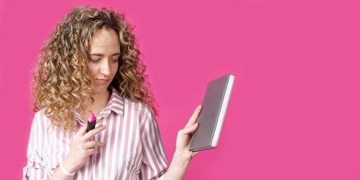 Fashionable woman in a striped shirt holding a diary and a marker. Isolated on pink background