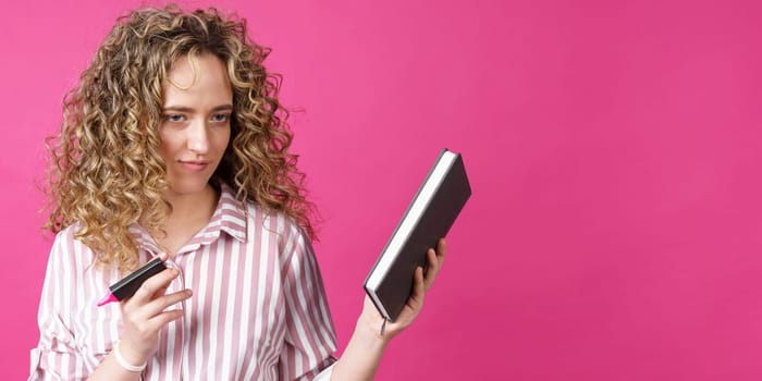 Fashionable woman in a striped shirt holding a diary and a marker. Isolated on pink background