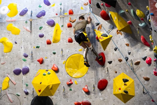 The climber trains on the artificial rock wall with insurance in bouldering gym, April 2022, Prague, Czech Republic.