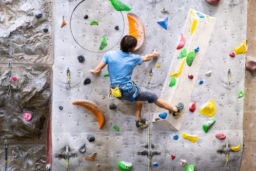 The climber trains on the artificial rock wall with insurance in bouldering gym, April 2022, Prague, Czech Republic.
