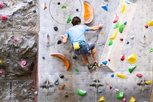 The climber trains on the artificial rock wall with insurance in bouldering gym, April 2022, Prague, Czech Republic.