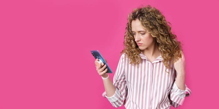 Fashionable woman in a striped shirt, reads a message on the phone. Isolated on pink background