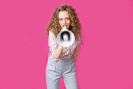 Young woman speaks into a megaphone. Isolated pink background. People sincere emotions lifestyle concept.