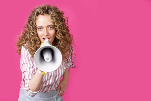 Young woman speaks into a megaphone. Isolated pink background. People sincere emotions lifestyle concept.