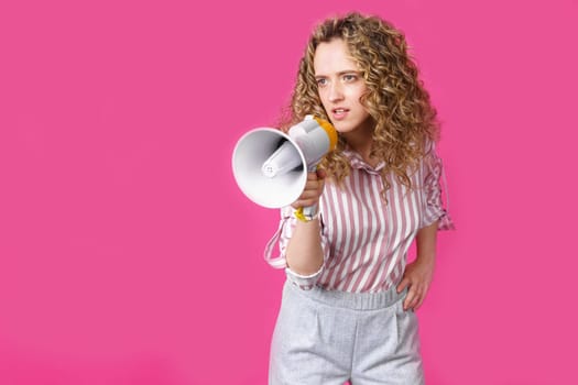 Young woman speaks into a megaphone. Isolated pink background. People sincere emotions lifestyle concept.