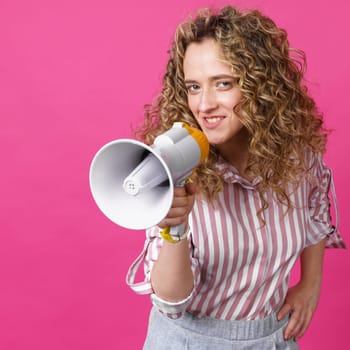 Young woman speaks into a megaphone. Isolated pink background. People sincere emotions lifestyle concept.