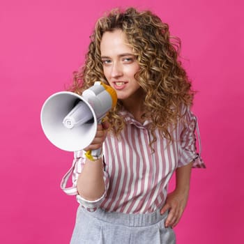 Young woman speaks into a megaphone. Isolated pink background. People sincere emotions lifestyle concept.