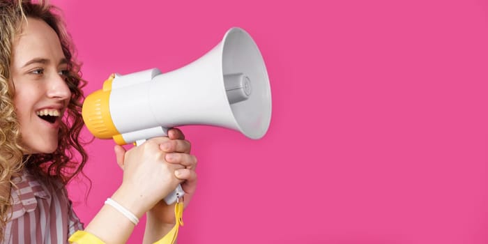 Young woman shouts into a megaphone. Isolated pink background. People sincere emotions lifestyle concept.