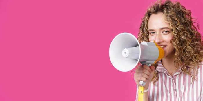 Young woman speaks into a megaphone. Isolated pink background. People sincere emotions lifestyle concept.