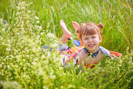 Portrait of little girl with Asian eyes in a meadow or field with grass and flowers on a sunny summer day