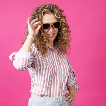 Portrait of a young, beautiful, healthy woman holding glasses and looking at the camera. Isolated on pink background.