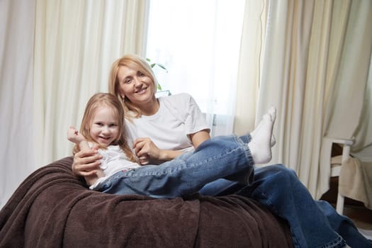 Happy loving family with mother and daughter having hugs in living room. Woman mom and small child girl inside of home