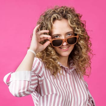 Portrait of a young, beautiful, healthy woman holding glasses and looking at the camera. Isolated on pink background.