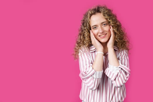 Portrait of a happy woman who holds her hands to her face and smiles. Isolated on a pink background.