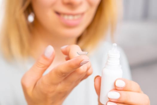Smiling woman holding a contact eye lens on her finger and eye drops in her hand. Inserting a corrective contact lens.