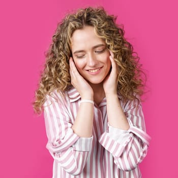Portrait of a happy woman who holds her hands to her face and smiles. Isolated on a pink background.
