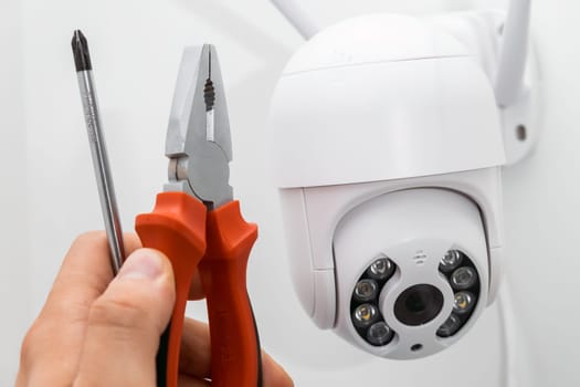 Technician installing CCTV camera using pliers and screwdriver outside of the building.