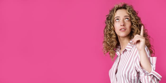 Young beautiful woman, amazed and surprised, looking up and pointing with fingers and raised hands. Isolated on pink background.