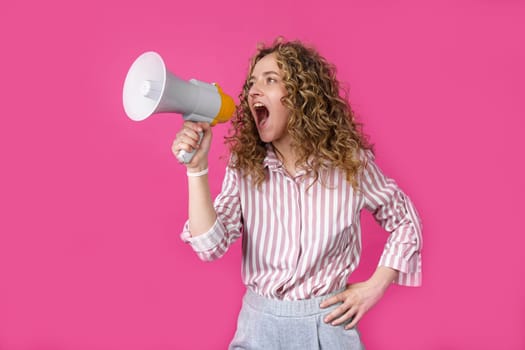 Young woman shouts into a megaphone. Isolated pink background. People sincere emotions lifestyle concept.