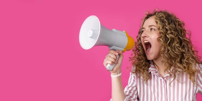 Young woman shouts into a megaphone. Isolated pink background. People sincere emotions lifestyle concept.