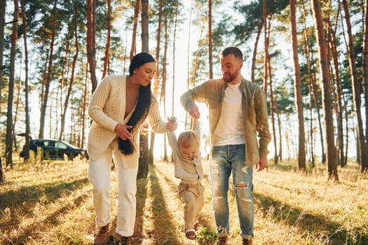 Holding little girl by hands. Happy family of father, mother and little daughter is in the forest.