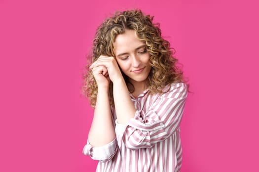 Happy contented woman holds her hands together near the face. Isolated on pink background