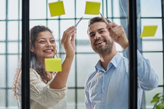 Creative professionals standing and discussing in office behind glass wall with sticky notes