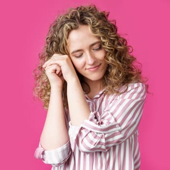 Happy contented woman holds her hands together near the face. Isolated on pink background