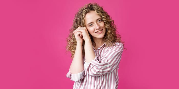 Happy contented woman holds her hands together near the face. Isolated on pink background