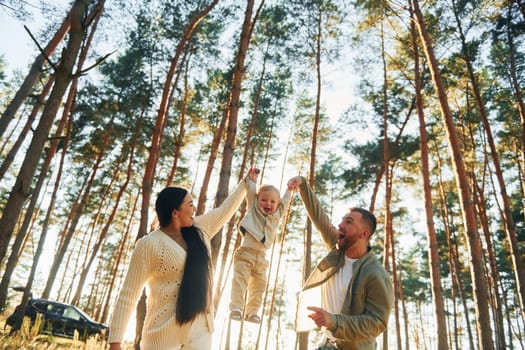 Holding little girl by hands. Happy family of father, mother and little daughter is in the forest.