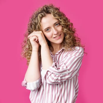 Happy contented woman holds her hands together near the face. Isolated on pink background