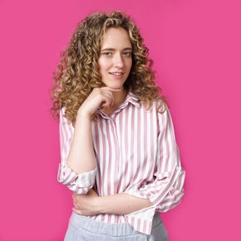 Happy contented woman holds her hands together near the face. Isolated on pink background