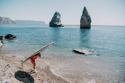 Close up shot of beautiful young caucasian woman with black hair and freckles looking at camera and smiling. Cute woman portrait in a pink bikini posing on a volcanic rock high above the sea