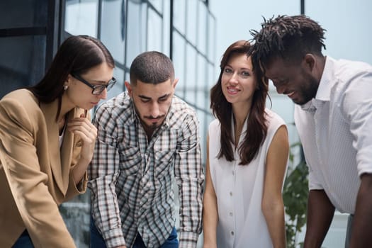 The concept of cooperation and brainstorming. Portrait of interracial friends gathered together, standing around a table in a classroom surrounded by books