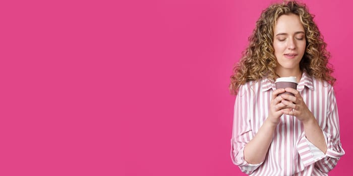 Young beautiful woman holding coffee in her hands. Isolated pink background