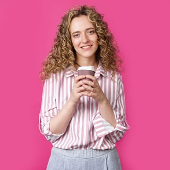 Young beautiful woman holding coffee in her hands and smiling. Isolated pink background