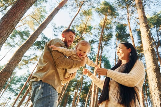 View from below. Happy family of father, mother and little daughter is in the forest.