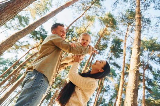 View from below. Happy family of father, mother and little daughter is in the forest.