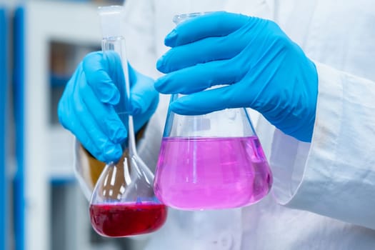 Scientist doing experiments with bright solutions in the flasks at the chemical laboratory. Researcher working in modern microbiology center.