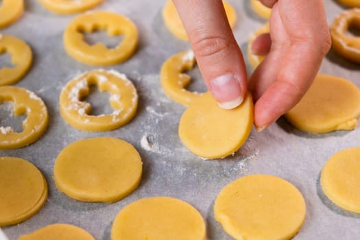 Close up woman hands put sugar cookies in the shape of angels on the baking paper ready for baking for St Valentines Day. Home made biscuits