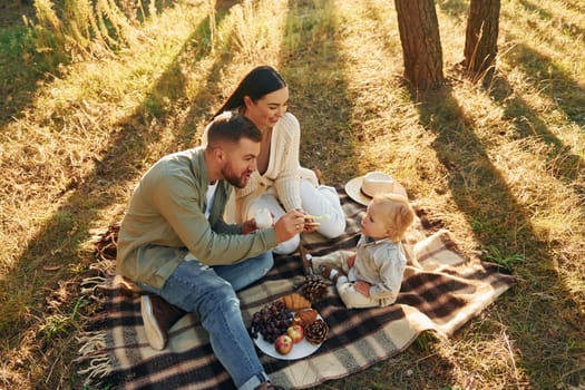 Eating some food. Happy family of father, mother and little daughter is in the forest.