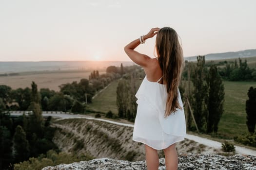 Romantic beautiful bride in white dress posing with sea and mountains in background. Stylish bride standing back on beautiful landscape of sea and mountains on sunset