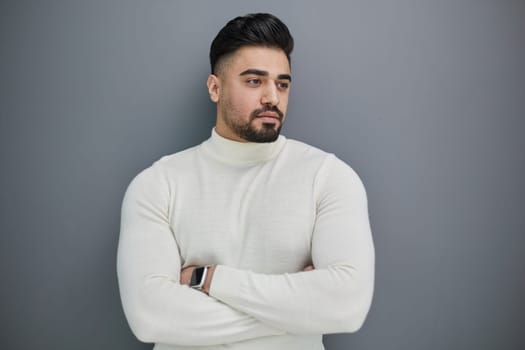 Portrait of a stylish man posing on a gray background with his arms crossed
